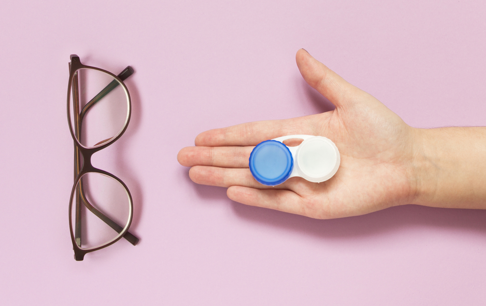 Glasses,And,Contact,Lens,Case,In,Human,Hand,On,Purple